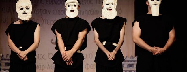 Cuatro actores y actrices de Teatro Paladio en escena, vestidos de negro y con máscaras griegas