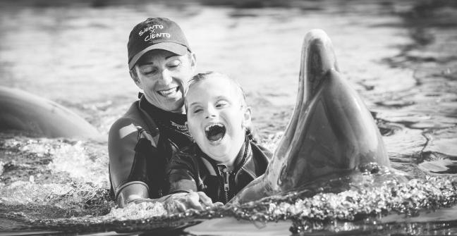 Fotografía del niño Ioan Inchusta feliz nadando con delfines y una monitora